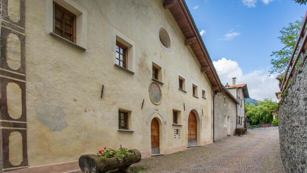A historic building with multiple windows and doors, a cobblestone courtyard, and a stone bench with flowers. - Pedranzini 23 in Bormio (Bormio)