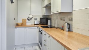 Une cuisine compacte avec des meubles blancs, un plan de travail en bois, un four à micro-ondes, un grille-pain et une bouilloire.