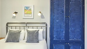 Une chambre à coucher avec un lit, deux lampes fixées au mur, un tableau encadré et une grande armoire bleue.