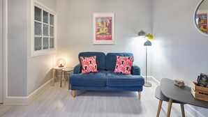 Une pièce avec un canapé bleu, une petite table, un lampadaire et une affiche accrochée au mur.