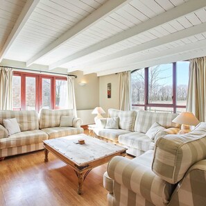 A spacious living room with a high ceiling, large windows, and a cozy arrangement of sofas and a coffee table.