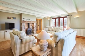A cozy living room with striped sofas, a fireplace, a television, and a stone wall.
