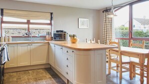 A modern kitchen with a large island, built-in cabinets, and a view through the window. - Host Stay The Coach House (Berwick-upon-Tweed)