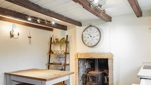 A rustic interior with a wooden table, a stone fireplace, and a wall clock.