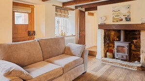 A cozy living room with a beige sofa, wooden flooring, a stone fireplace, and exposed wooden beams on the ceiling.