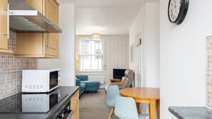 A compact kitchen with modern appliances, a dining area with two chairs, and a living space with a sofa and a TV. - Host Stay Abbey View (Whitby)