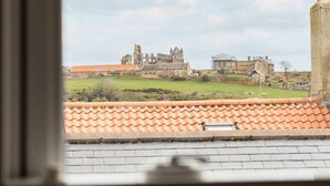A view of a historic building complex with ruins and a modern structure, viewed from a window with a tiled roof. - Host Stay Abbey View (Whitby)