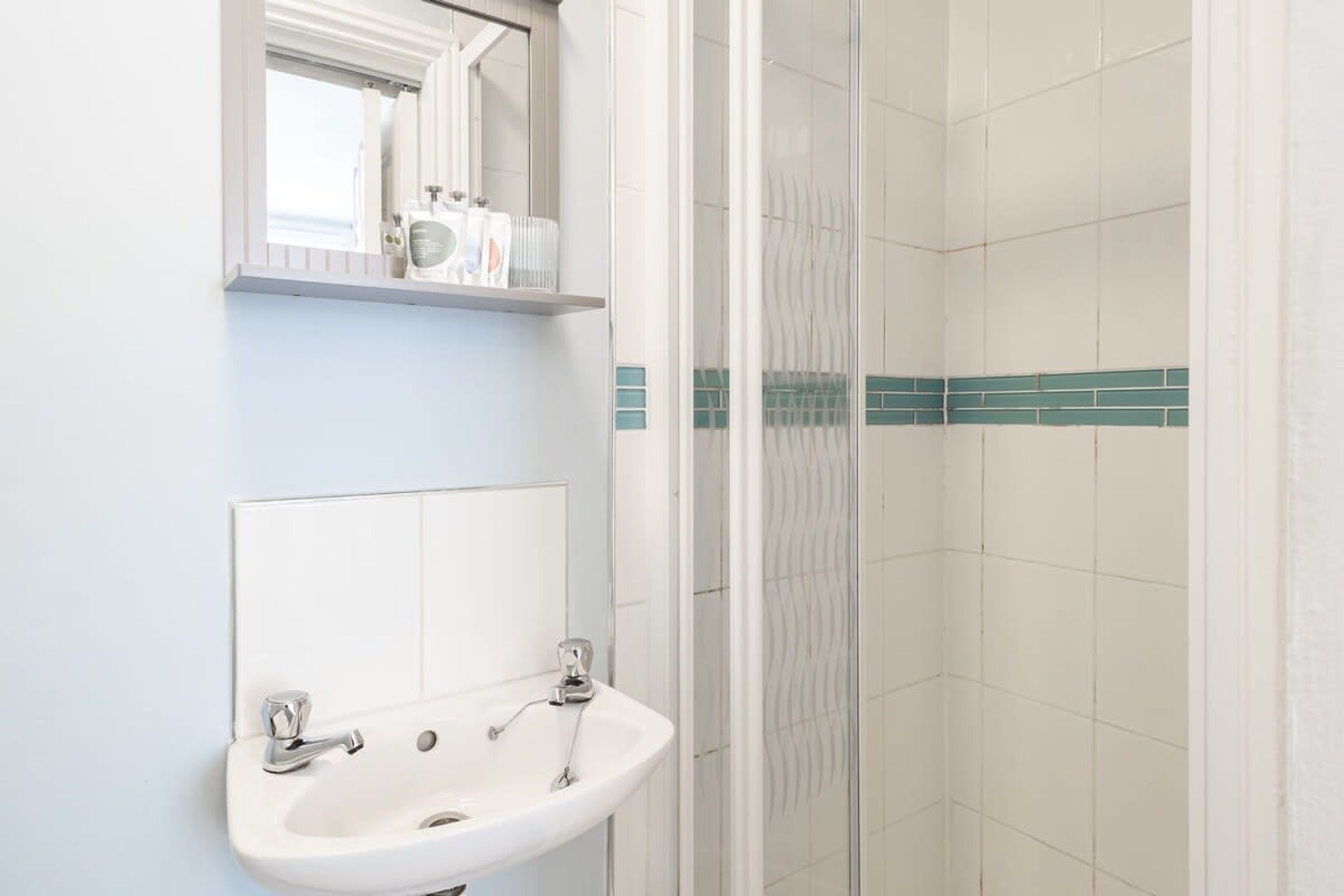 A bathroom with a sink, mirror, and shower.