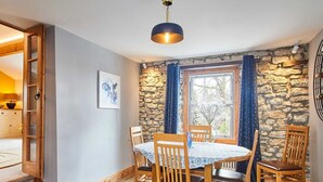 Et spiseområde med en stenvæg, træstole, et rundt bord og en blå måtte.