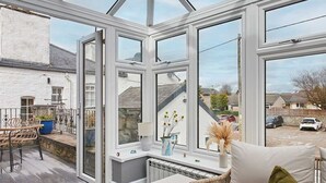 A conservatory with a glass roof, a seating area with a sofa and chairs, a small table with decorative items, and a view of the outside. - Host Stay Lime Tree House (Carnforth)