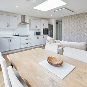 Une cuisine moderne avec des meubles blancs, une table à manger en bois et un mur à l’aspect pierre.