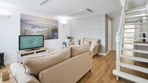 A modern living room with a beige sofa, a flat-screen TV, a painting, and a staircase. - Host Stay Emilyn House (Sunderland)