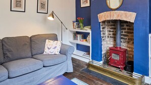 A living room with a grey sofa, a blue wall, a red wood-burning stove, and framed pictures on the wall.