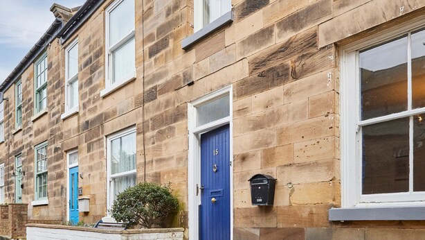 A row of terraced houses with stone facades, a blue door, and a mailbox.