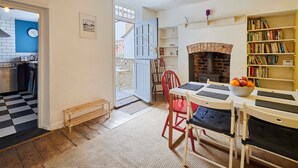 A cozy kitchen with a checkered floor, a dining area with a table and chairs, a bookshelf, and a fireplace.