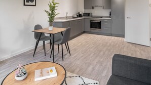 A modern kitchen with grey cabinets, a microwave, and a sink. There is a dining area with a table and chairs, and a potted plant. - Host Stay 36 Waterside Place (Taunton)