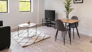 A modern living room with a TV, a dining table with chairs, a potted plant, and two pendant lights. - Host Stay 36 Waterside Place (Taunton)
