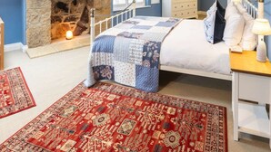 Een slaapkamer met een stenen openhaard, een bed met quilt, een dressoir en een nachtkastje.