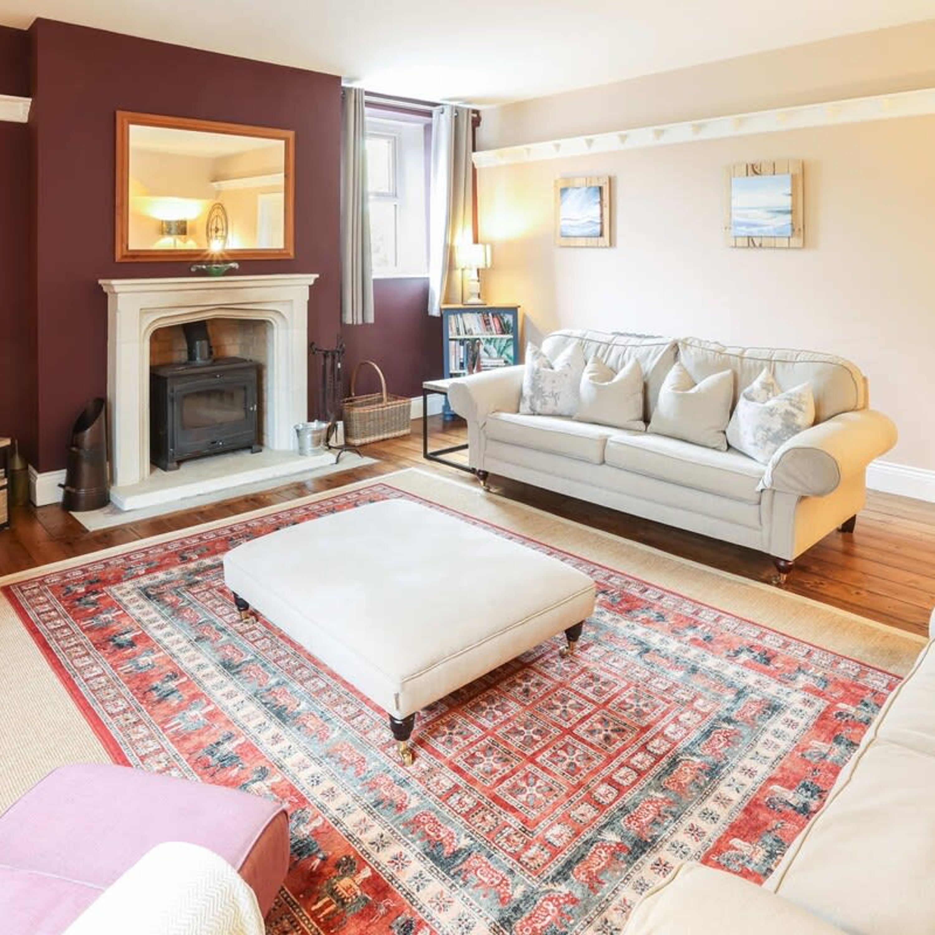 Una sala de estar con chimenea, un sofá, un reposapiés y una alfombra estampada.