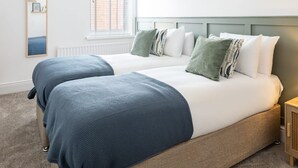 Une chambre avec deux lits, une fenêtre avec des stores, un radiateur et une table de chevet.