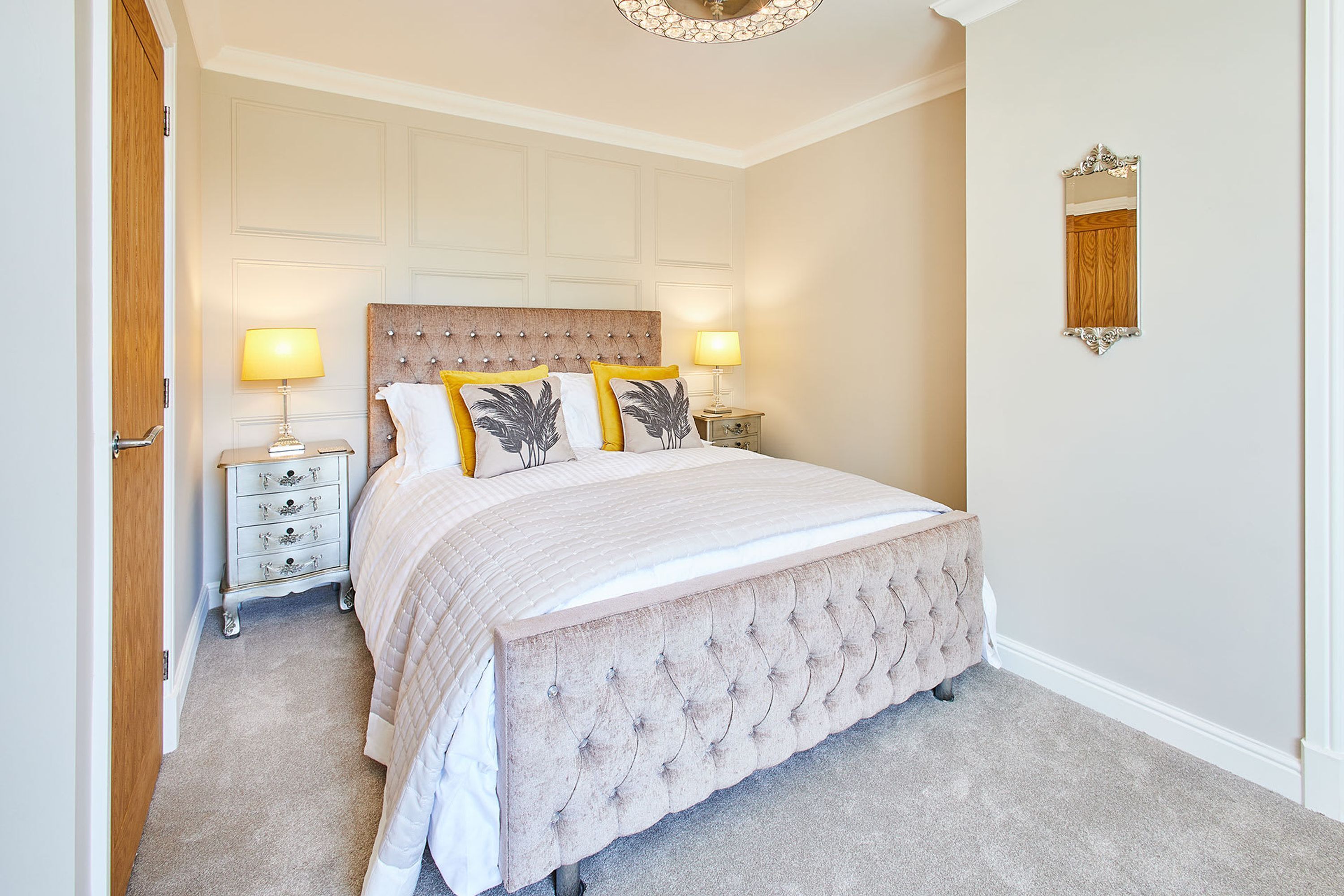 A bedroom with a large bed, two bedside tables, a wooden headboard, and a mirror on the wall.