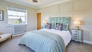 Een slaapkamer met een groot bed, een nachtkastje, een lamp, een radiator, een raam met gordijnen en een deur.