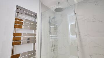 Een moderne badkamer met een glazen douchecabine, een handdoekrek van hout en metaal en marmeren wanden.