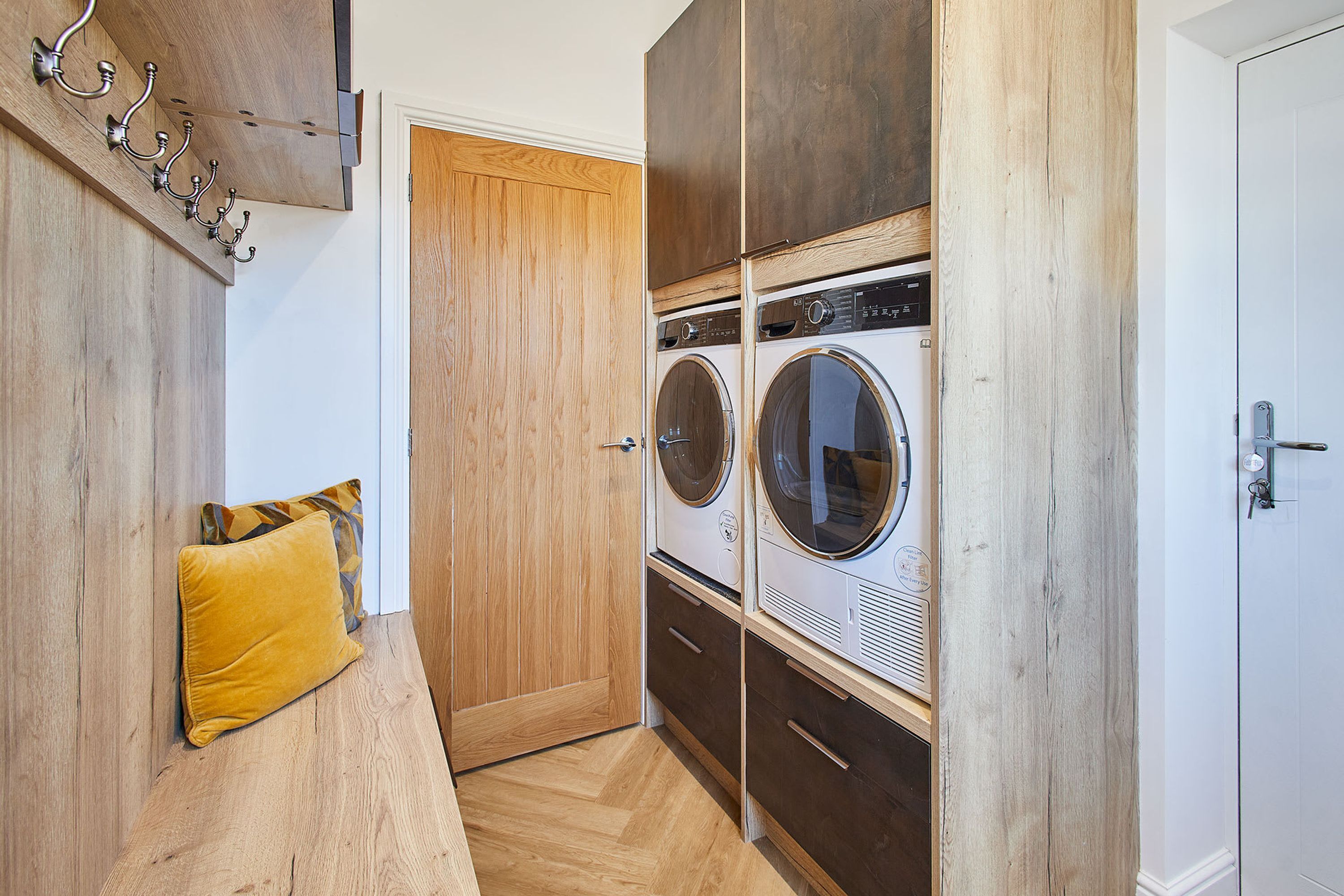 A laundry room with a wooden bench, a yellow pillow, and a door.