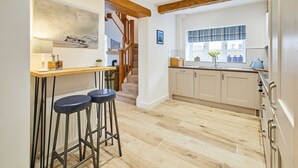 Une cuisine avec un plancher en bois, un coin bar avec des tabourets et une fenêtre agrémentée d’une lambrequin à rayures.