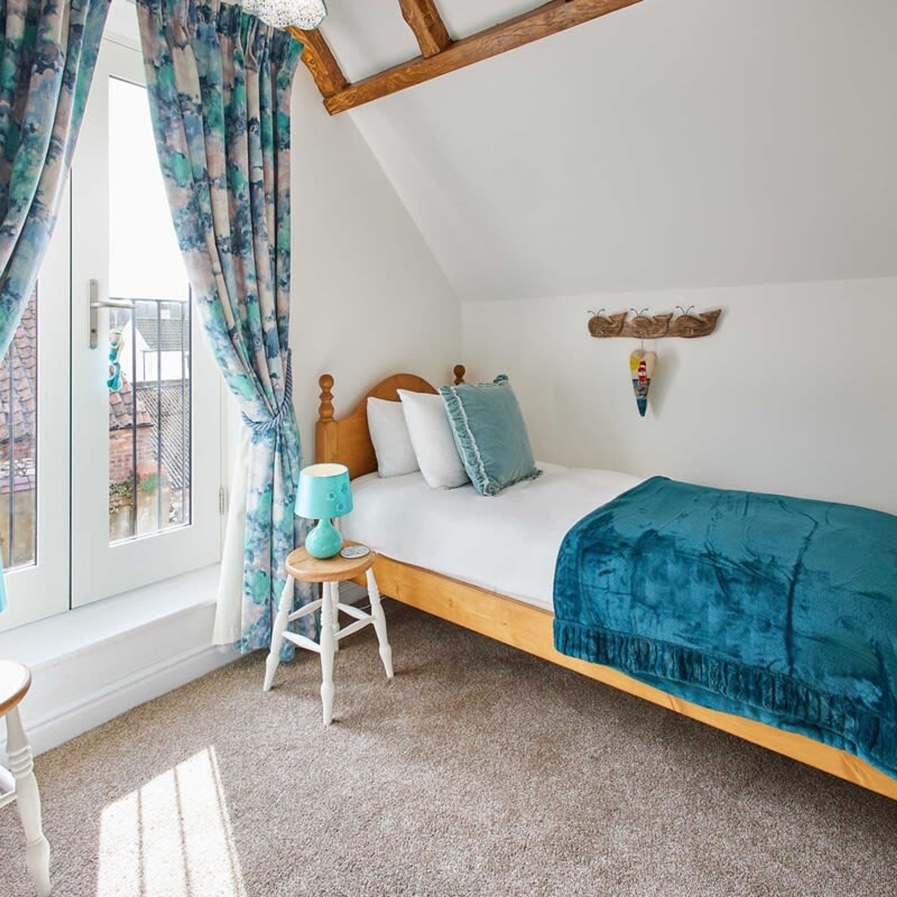 A bedroom with a loft bed, a small stool, a lamp, and a window with curtains.