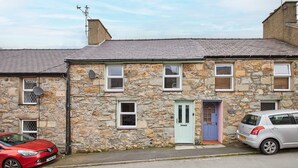 A stone house with a blue door, a red car parked on the street, and a silver car parked on the driveway. - Host Stay Trefor Cottage (Caernarfon)