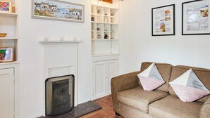 A living room with a fireplace, wooden beams, a sofa with cushions, and a rug. - Host Stay Trefor Cottage (Caernarfon)