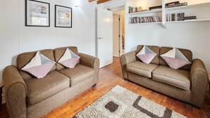 A living room with two sofas, a wooden floor, a white door, and a bookshelf with DVDs. - Host Stay Trefor Cottage (Caernarfon)