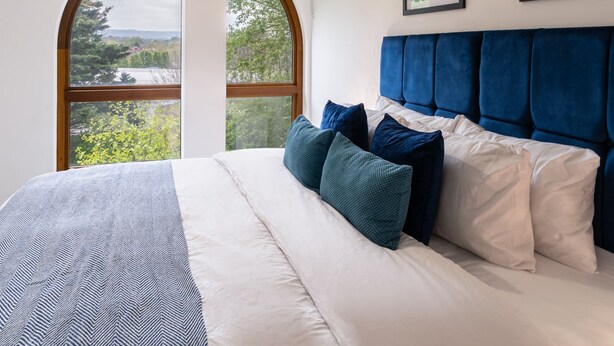 Ein Schlafzimmer mit einem großen Bett, Blick durch ein Fenster und einer Deckenleuchte.