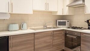 Una cocina moderna con armarios blancos, un microondas de acero inoxidable, una estufa a gas y un lavavajillas.