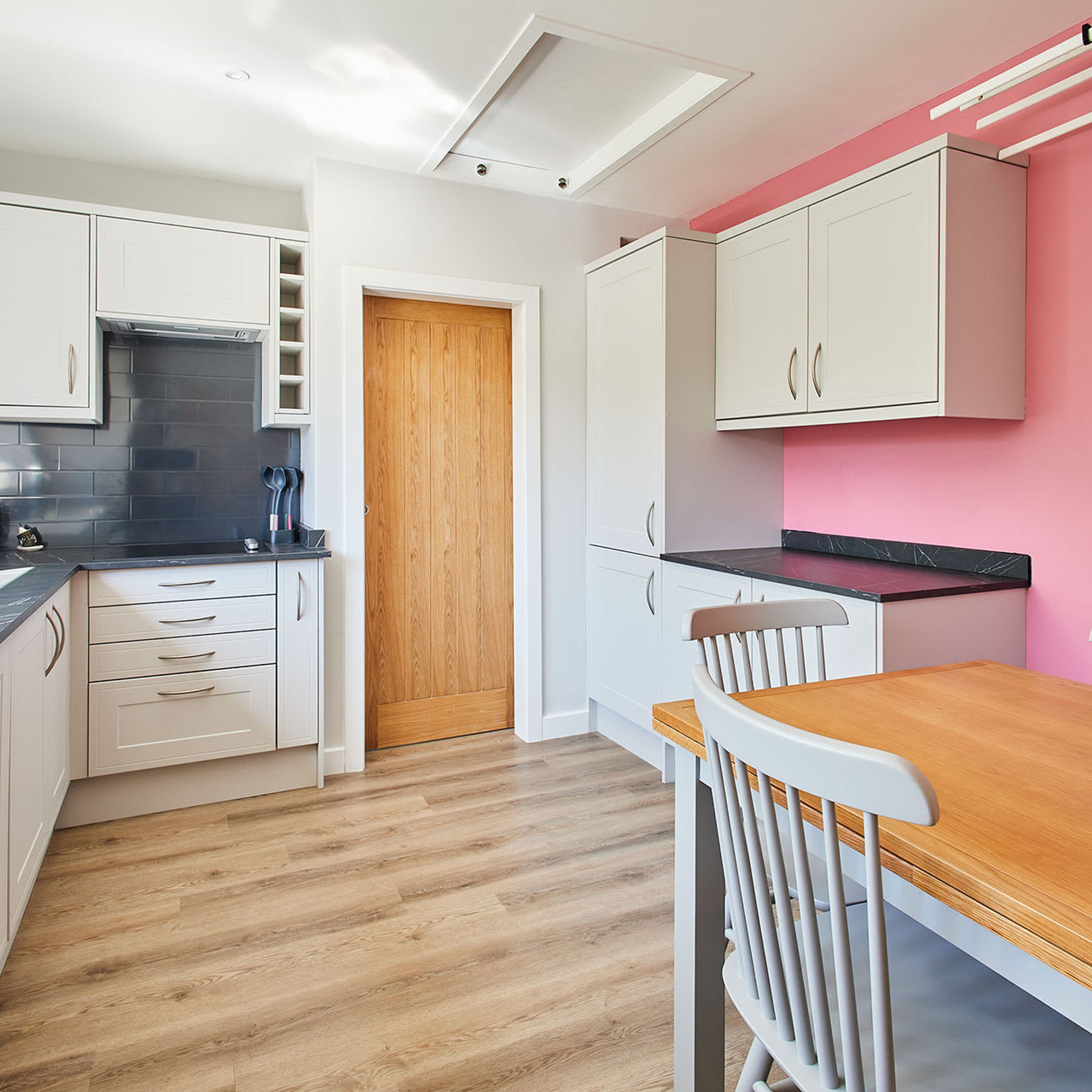 A modern kitchen with white cabinets, a wooden door, and a dining area with a wooden table and white chairs.