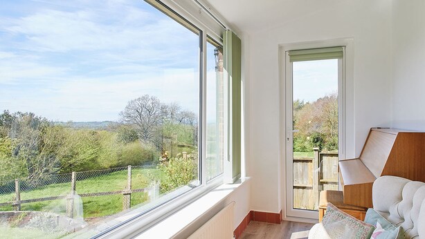 A room with a large window, a wooden bench, a white sofa with cushions, and a door leading outside. - Host Stay Manifold (Northallerton)