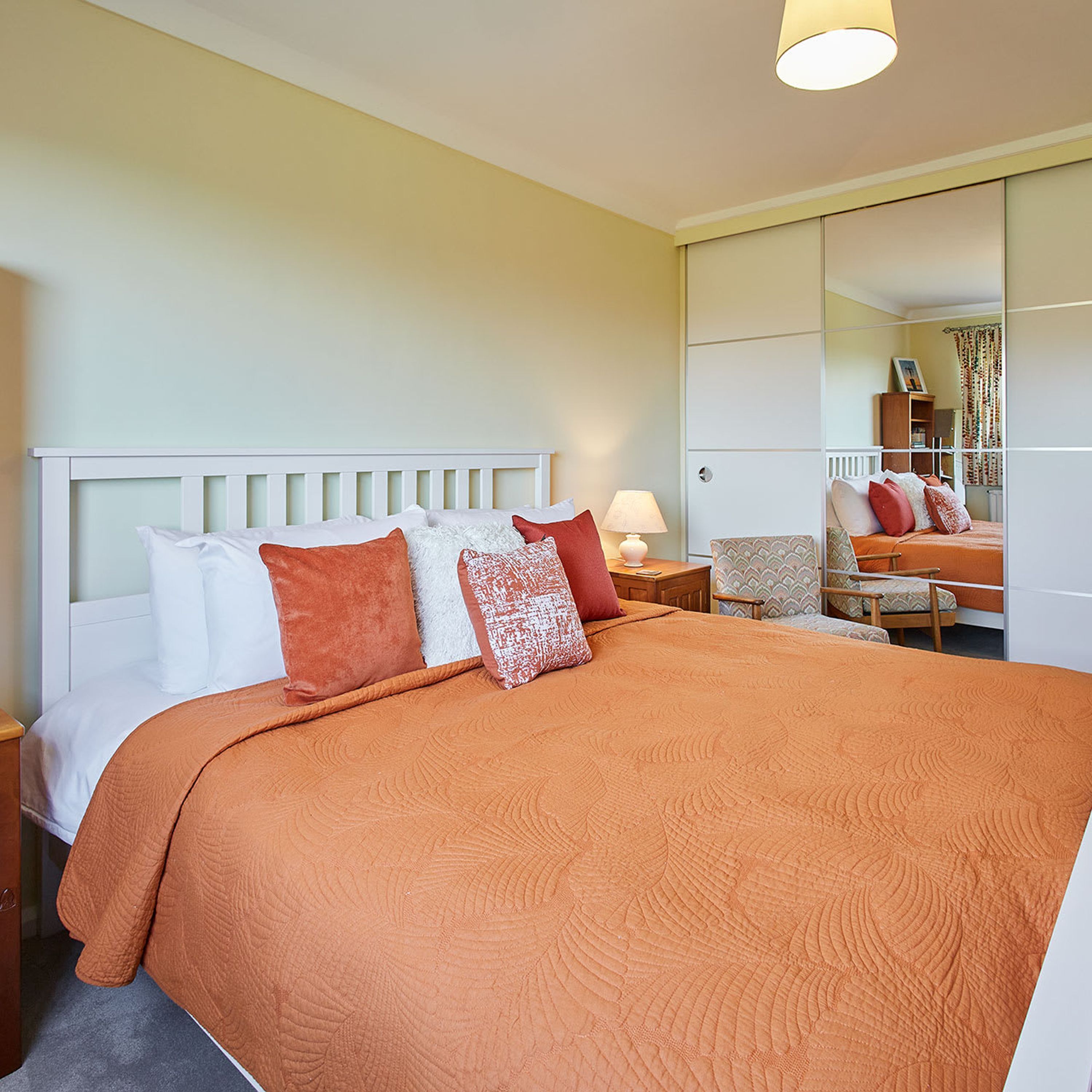 A hotel room with a large bed, a nightstand, a chair, a desk, and a mirror.