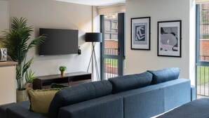 A modern living room with a large dark blue sofa, a flat-screen TV mounted on the wall, and two framed abstract artworks on the wall. - Host Stay Richmond Place 003 (Liverpool)