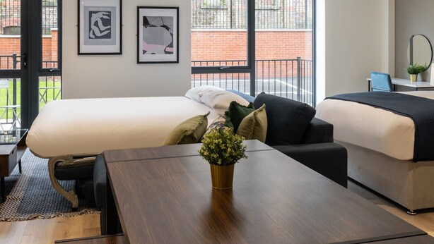 A modern hotel room with a large bed, a sofa, a wooden table, and two framed pictures on the wall. - Host Stay Richmond Place 003 (Liverpool)