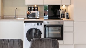 Cocina moderna con lavadora integrada, horno y microondas. Cuenta con un comedor con mesa y sillas.