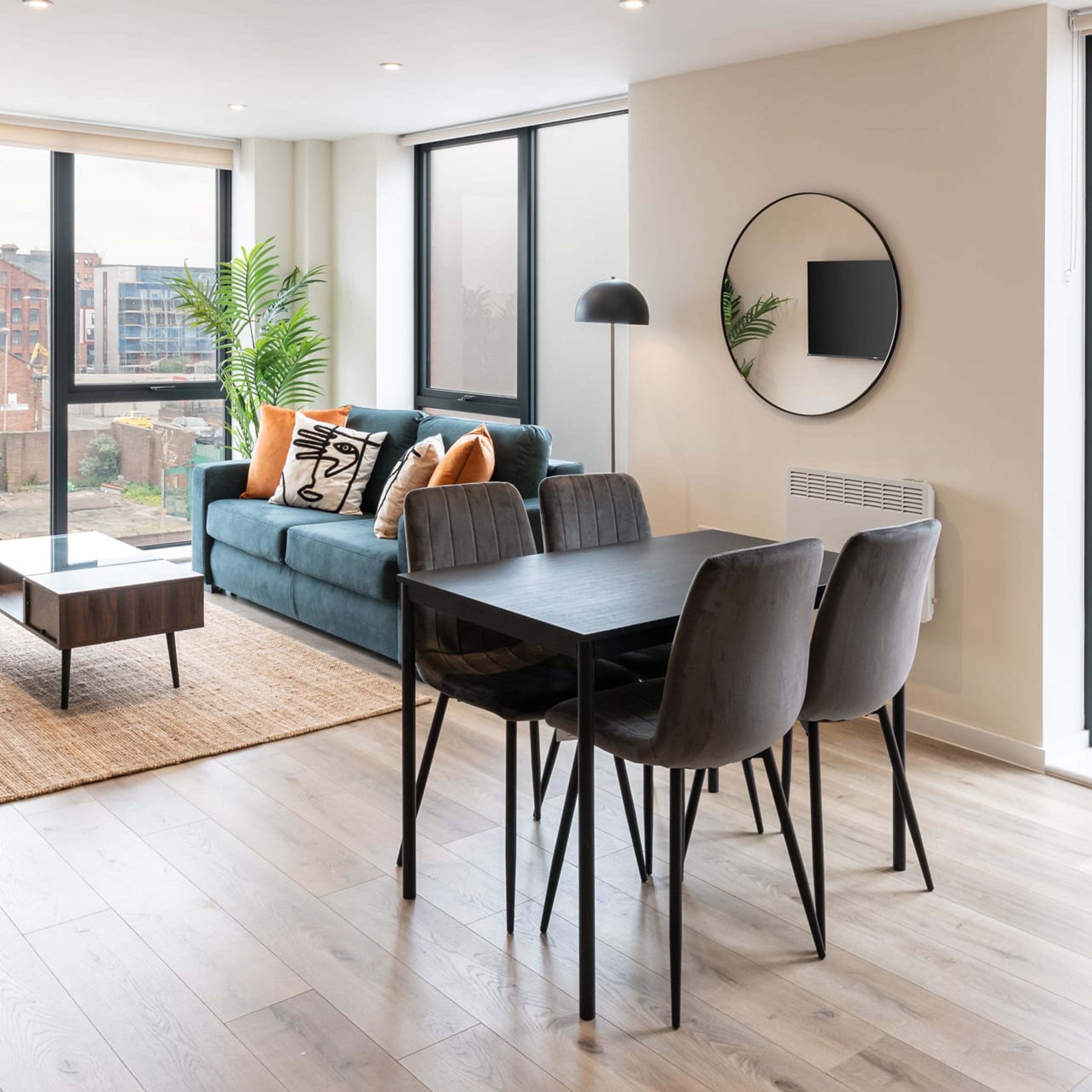 A modern living room with a sofa, a dining table with chairs, a floor lamp, and a large window with a view of buildings.