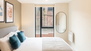 A bedroom with a large bed, a window with a view of a brick building, a round mirror, and a radiator. - Host Stay Richmond Place 102 (Liverpool)