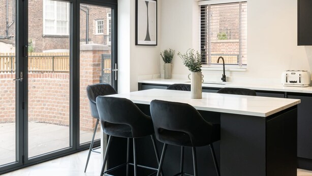 A modern kitchen with a large island, black bar stools, and a view of the outside.
