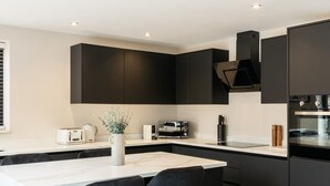 A modern kitchen with a central island, black bar stools, and a coffee machine.