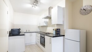 Uma cozinha moderna com armários brancos, bancada preta, fogão, forno, geladeira e um relógio de parede.