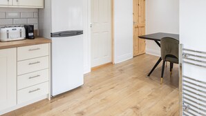 Eine kleine Küche mit weißen Schränken, einem integrierten Kühlschrank, einem Toaster und einer Kaffeemaschine.