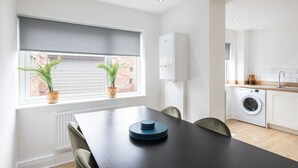 Eine moderne Küche mit Einbauwaschmaschine, einem Esstisch mit Stühlen sowie einem Fenster mit Jalousien und Topfpflanzen.