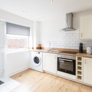 A modern kitchen with a washing machine, oven, and a window with a view of a brick wall. - Host Stay Milbanke House (Seaham)