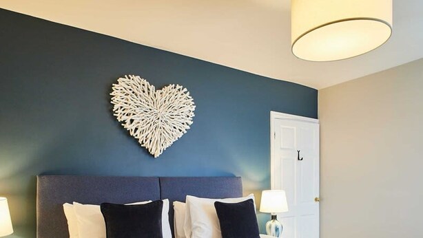 A hotel room with a large bed, a heart-shaped wall decoration, and a door.